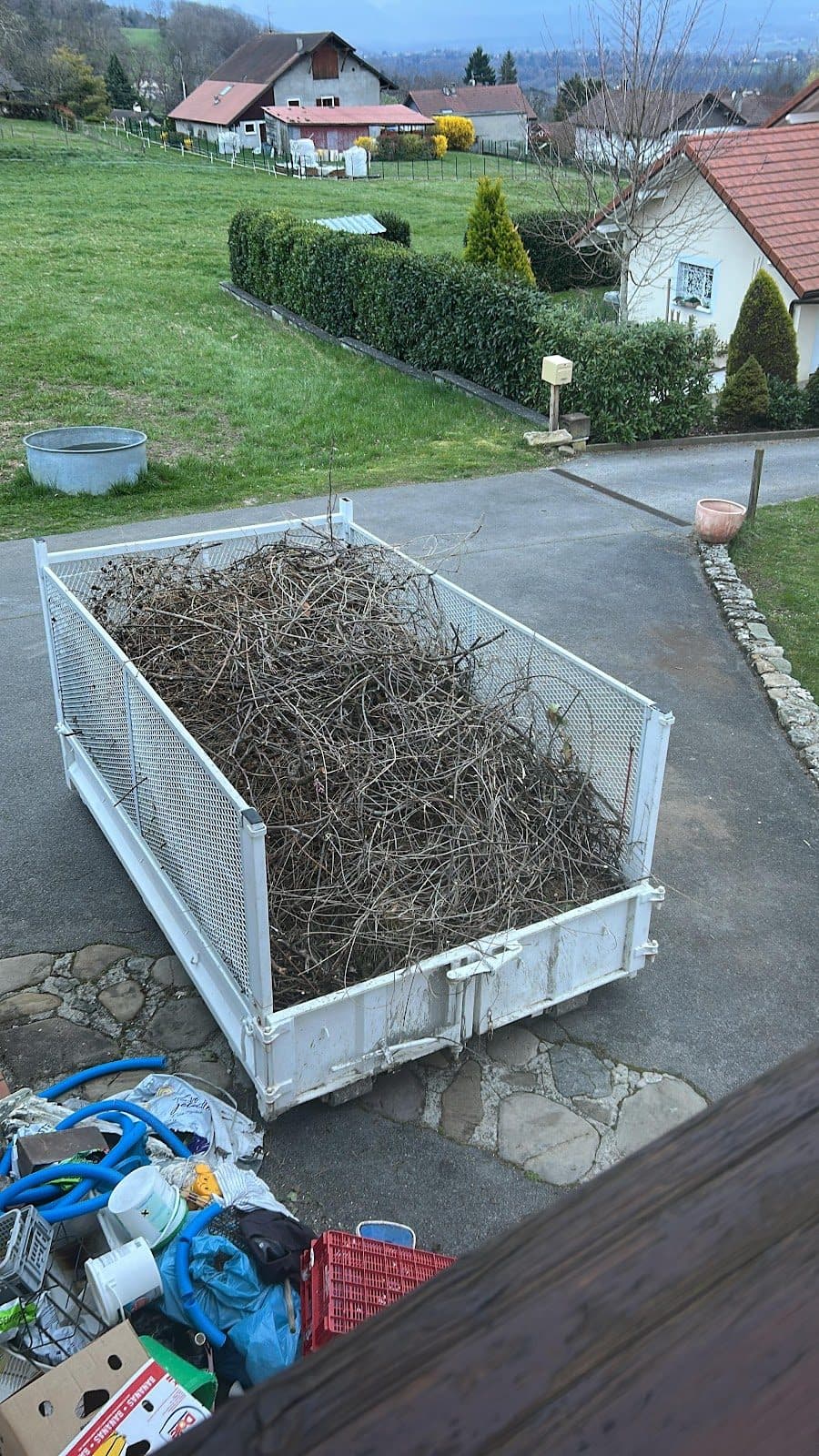 Benne remplie de déchets verts devant une maison
